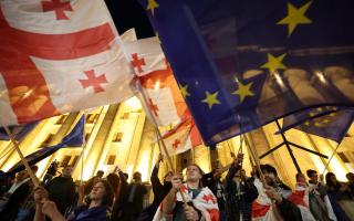 TOPSHOT - Protesters wave Georgian national and European flags during a demonstration outside the parliament building as they protest against a draft bill on 