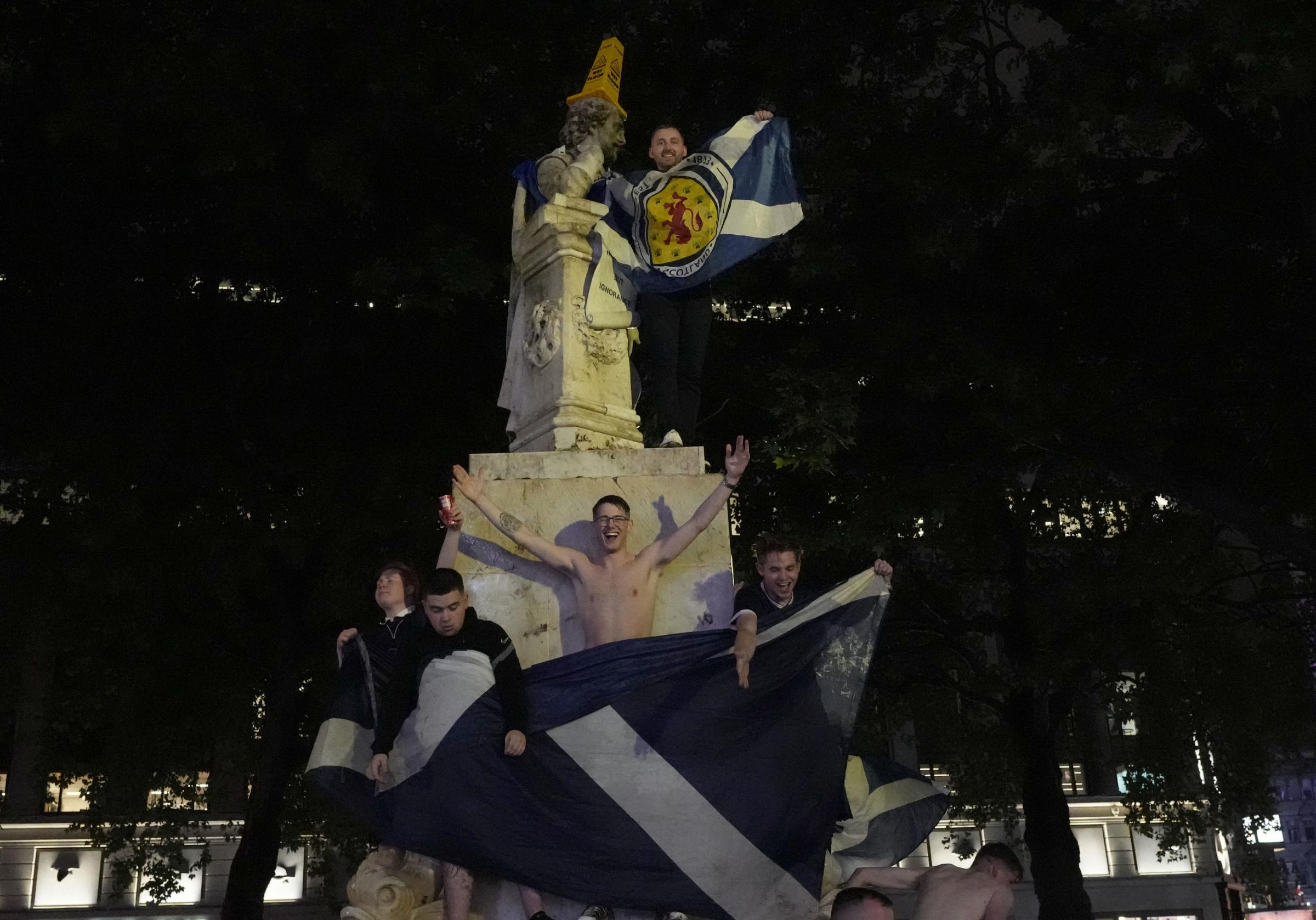 A Scotland supporter holds a flag as he stands on the statue to William Shakespeare in Leicester Square in London, Friday, June 18, 2021 after the Euro 2020 soccer championship group D match between England and Scotland at Wembley Stadium. The match