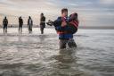 A migrant carries a child as he runs to board a smuggler's boat on the beach of Gravelines, near Dunkirk (Photo by Sameer Al-Doumy/AFP via Getty Images).