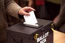 Person places their vote in a ballot box at a polling station..