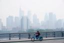 A person cycles past the skyline in Philadelphia shrouded in haze (Matt Rourke/AP)