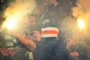 A Celtic fan wearing a balaclava sets off two flares at a match