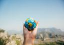 A person holding a planet Earth against a mountainous landscape. Credit: Canva