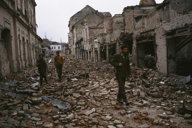 Yugoslavian soldiers and Serb paramilitaries, including Zeljko 'Arkan' Raznatovic, walk past bombed buildings riddled with bullet holes and streets filled with rubble after a three-month battle