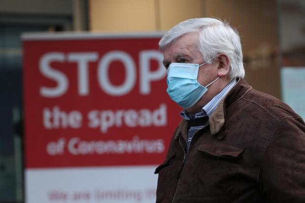 The National: A man wearing a face mask walks past a coronavirus advice sign