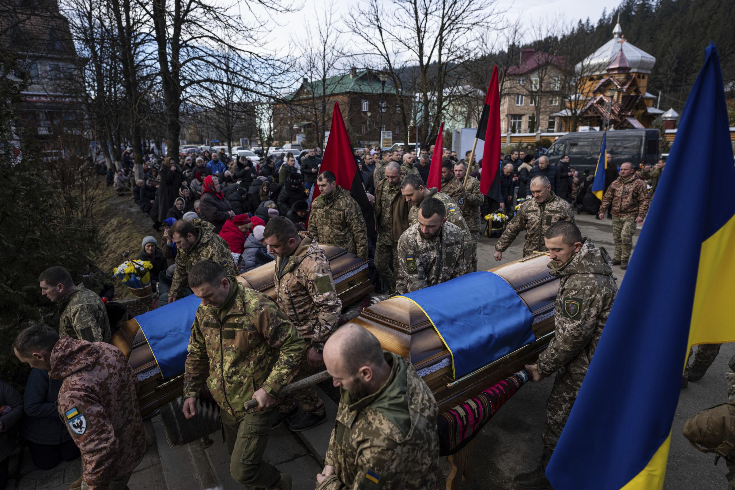 Ukrainian servicemen carry the coffins of their killed comrades Vasyl Medviychuk and Dmytro Dosiak during a funeral ceremony in Verkhovyna, Ukraine, Thursday, Dec. 28, 2023. (AP Photo/Evgeniy Maloletka).