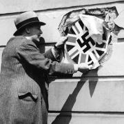 A man reveals the image of a Union Jack with a swastika superimposed on the wall of a house in Haverstock Hill, near Hampstead, in 1953