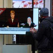 Passers-by look at a tv screen in a Glasgow shop showing First Minister Nicola Sturgeon making a Covid-19 statement. Photo: PA