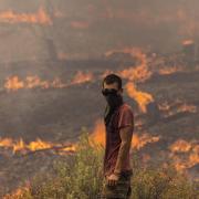 A man stands ready to fight flames as they engulf a hillside on July 27, 2023 in Rhodes, Greece