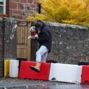 A man lifts his dog over a flood defence barrier erected on Church Street in Edzell, Angus