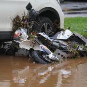 A moped covered in debris lies against a vehicle after being knocked over by flood water in Brechin