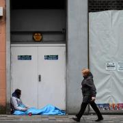 A woman walks past a homeless person lying in a doorway in Glasgow city centre