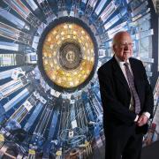 Nobel Prize winning physicist Peter Higgs pictured in front of a photograph of the Large Hadron Collider