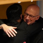 John Swinney, Scotland's next first minister, embraces his predecessor Humza Yousaf in the Holyrood chamber