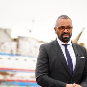 Home Secretary James Cleverly standing in front of a discarded migrant boat in Lampedusa Port in Italy