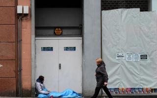 A woman walks past a homeless person lying in a doorway in Glasgow city centre
