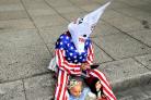 A woman dressed in a Stars and Stripes motif outfit and a klansman hood, takes part in a protest against immigration policies in front of the United States Embassy in Mexico City